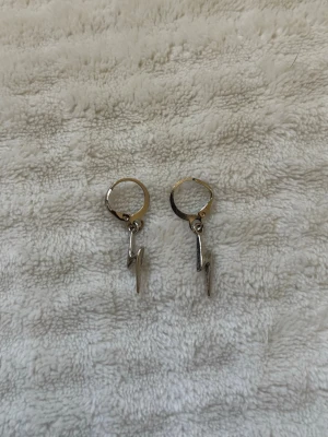 Silverfärgade blixtörhängen - Säljer ett par coola örhängen i silverfärg med hängande blixtformade berlocker. Örhängena har enkel ringdesign och är perfekta för dig som gillar edgy accessoarer. Märke saknas.