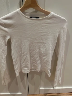 Vit långärmad topp från Miss Selfridge - Klassisk vit långärmad topp från bikbok i ribbad bomullsmix. Enkel och stilren design med rund halsringning och figurnära passform. 