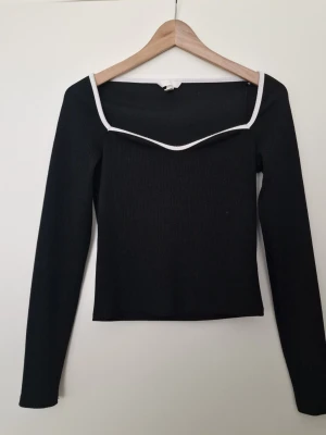 H&M svart långärmad topp med vit kant S - H&M Svart långärmad topp med ribbad struktur och vit kant längs den fyrkantiga urringningen. Snygg och stilren modell som sitter figurnära och har en modern look. Storlek S. Perfekt skick.