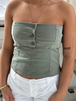 Grön tubtopp med knappar - Snygg grön tubtopp, helt ny med lapp kvar, den var lite för stor så därför säljer jag😊❤️