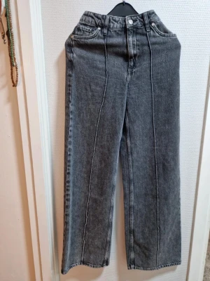 Grå raka jeans från Mango - Snygga grå jeans från Mango med raka ben och markerad pressveck framtill. Jeansen har hög midja, klassiska fem fickor och bälteshällor. Perfekta för en trendig och avslappnad look.