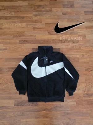 Nike Reversibel Jacka - 🖤🖤 Nike Reversibel Jacka – Storlek M 🖤 Exklusiv Nike-jacka i storlek M med två stilar i ett: svart sherpa-fleece med vit swoosh och Dri-FIT-teknologi, eller svart glansigt, vindtätt tyg med vit Nike-logga. Hög krage, hel dragkedja, ribbade ärmslut och fåll för bättre passform. Perfekt för sport och vardag. Ny med taggar. ✨ Detaljer: M (liten i storlek), reversibel, mjuk fleece + vindtätt tyg, Dri-FIT, nyskick. 📦 Snabb leverans – kontakta vid frågor!