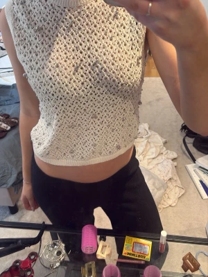 Vit stickad pärlprydd linnetopp - Säljer en vit stickad linnetopp med pärlor. Toppen är ärmlös, croppad och har ett öppet hålmönster som ger en luftig känsla. Perfekt för dig som vill ha en unik och trendig topp till sommaren. L men sitter som s