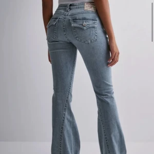 Ljusblå bootcut jeans från True Religion - Säljer ett par ljusblå bootcut jeans från True Religion med klassiska kontrastsömmar och dekorativa ficklock bak. Jeansen har låg midja, fem fickor och är tillverkade i mjuk denim med stretch. Perfekta för en avslappnad men trendig look. Säljer för att de inte kommer till användning längre, men de är sparsamt använda.