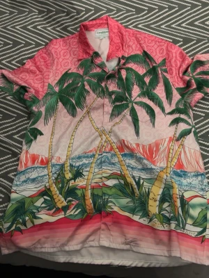 Färgglad palmmönstrad skjorta - Säljer en färgglad skjorta från Casablanca med tropiskt palmmönster i grönt, rosa och vitt. Skjortan har korta ärmar och knappar framtill. Perfekt för dig som vill sticka ut med en unik och somrig look.