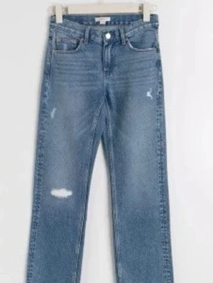 Blå raka jeans med slitningar - Säljer ett par blå jeans med raka ben och snygga slitningar på låret och knät. Jeansen har klassisk femficksmodell, normal midja och stängs med knapp och dragkedja. Perfekta för en avslappnad och trendig look.Obs. Den stora slitningen vid knät har blivit lösare och är som ett hål kan skicka bild vid intresse 