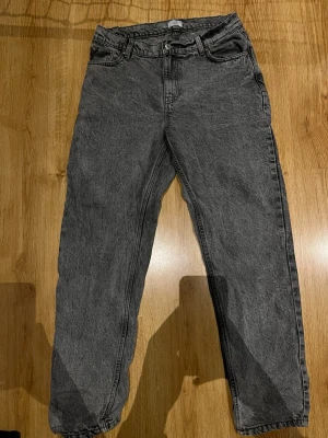 Grå mom jeans med hög midja - Säljer ett par grå jeans med raka ben. Jeansen har klassisk femficksdesign och är tillverkade i ett tvättat denimtyg som ger en cool vintagekänsla. Perfekta att styla med sneakers.