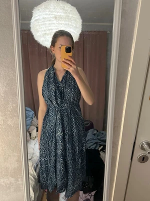 Blåmönstrad halterneckklänning - Snygg blå klänning med vitt mönster och halterneck. Klänningen har en luftig passform och är ärmlös, perfekt för varma dagar. Midjebandet ger en fin siluett och tyget känns lätt och bekvämt mot huden. Köpt i Indien.