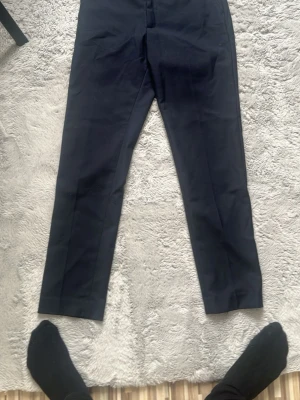 Svarta kostymbyxor med pressveck - Säljer ett par stilrena svarta kostymbyxor med pressveck och smal passform. Byxorna har diskreta fickor bak och är perfekta för en clean och uppklädd look. Materialet ser ut att vara en klassisk kostymblandning som ger en snygg siluett.