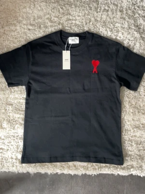 Ami paris t shirt - Snygg svart t-shirt från Ami Alexandre Mattiussi med ett ikoniskt rött hjärta och bokstaven A broderat på bröstet. Klassisk passform och rund halsringning. Tillverkad i mjuk bomull som känns skön mot huden.