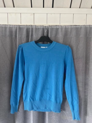 Blå stickad tröja Saint Tropez - Snygg blå stickad tröja från Saint Tropez med rund halsringning och ribbade muddar. Tröjan har puffade axlar som ger en trendig siluett och är tillverkad i ett mjukt material. Perfekt för dig som vill ha en enkel men stilren look.