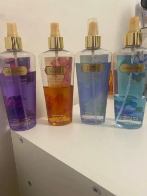 Victoria's Secret body mists 4-pack - Fyra olika body mists från Victoria's Secret: Love Spell (lila), Coconut Passion (gul/orange), Secret Charm (ljusblå) och Aqua Kiss (blå). Flaskorna är genomskinliga med guldfärgade spraymunstycken och etiketter. Varje flaska rymmer 250 ml och har blommiga och fruktiga doftnoter.