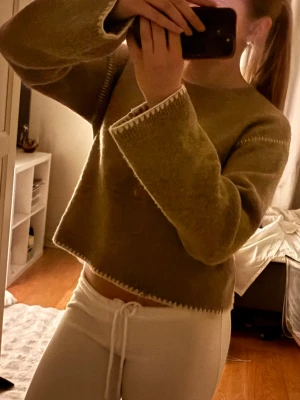 Beige fluffig tröja med vida ärmar och speciell sömn - Mysig beige tröja med fluffig textur och vida ärmar. Tröjan har dekorativa sömmar i vitt längs kanterna och är något croppad i modellen. Perfekt för dig som gillar en avslappnad och trendig stil. Storlek 158/164 men passar absolut både en xs eller S, jag har vanligtvis S