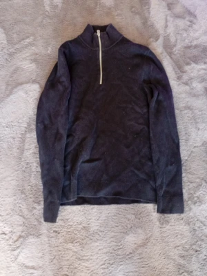 Mörkblå ribbad tröja med halvzip - Mörkblå långärmad tröja med ribbad struktur och hög krage. Tröjan har en vit halv dragkedja framtill som ger en sportig touch. Perfekt för lager-på-lager och enkel att matcha med olika outfits.