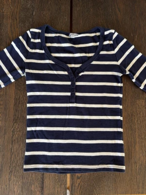 Randig topp från Subdued, marinblå/vit - Säljer en marinblå och vit randig topp från Subdued. Modellen har halvlånga ärmar, djup rundringning och knappar framtill. Tillverkad i mjukt, stretchigt material som sitter snyggt på kroppen. Perfekt för en avslappnad och trendig look. Storlek M men passar lite mer som en S.