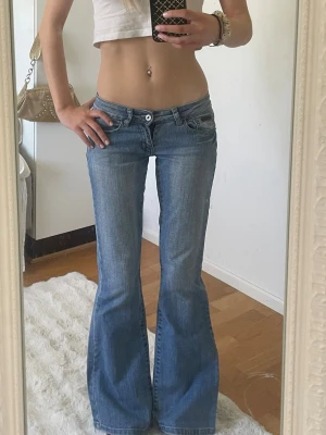 Blå bootcut jeans låg midja - Säljer ett par blå bootcut jeans med låg midja och klassiska fem fickor. Jeansen har en snygg tvätt och utsvängda ben, perfekta för en trendig och avslappnad look. Materialet är denim i bomull. Passar dig som gillar 00-talsstil.