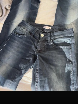 lågmidjade bootcut jeans - Snygga mörkblå bootcut jeans med slitningar och silverfärgade nitar längs fickorna. Bakfickan har en cool broderad hand-symbol. Klassisk femficksmodell med knapp och dragkedja. Perfekta för dig som vill ha en unik touch på din denimstil.