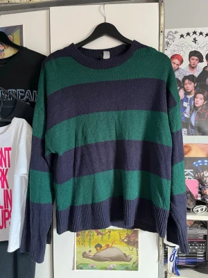 Randig stickad tröja i grönt och svart - Säljer en oversized stickad tröja med breda gröna och svarta ränder. Tröjan har rund halsringning, långa ärmar och ribbade muddar vid ärmslut och nederkant. Perfekt för en avslappnad och trendig look.