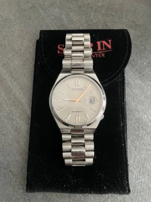 Citizen Champange Dial - Stilren automatisk klocka från Citizen i silverfärgat rostfritt stål. Klockan har en klassisk länkarmband, vit urtavla med datumvisning och tydliga indexmarkeringar. Baksidan har ett transparent fönster som visar urverket. Perfekt för dig som gillar tidlös design. 40mm Nypris 3498kr kvitto finns. 
