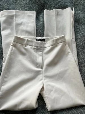 Vita kostymbyxor från Zara - Snygga vita kostymbyxor från Zara med en slits. Byxorna är högmiddajde och är långa i benen. Jag är 174 och byxorna går hela vägen ner🩷 dock är det en fläck på byxbenet längst ner på baksidan av byxorna (bild 3)