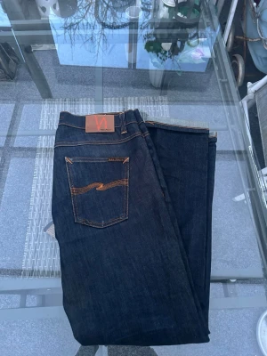 Nudie Jeans Lean Dean Dry 16 Dips – W33 L32 Raw Denim - Säljer ett par Nudie Jeans Lean Dean Dry 16 Dips i storlek W33 L32. Klassiska mörkblå raw denim jeans i premiumkvalitet.  Modellen Lean Dean är en populär slim/tapered fit som sitter snyggt över låren och smalnar av nedåt. Perfekta för både vardag och mer uppklädd stil.  Detaljer: • Modell: Lean Dean Dry 16 Dips • Storlek: W33 / L32 • Färg: mörkblå (raw / dry denim) • Material: 99% ekologisk bomull, 1% elastan • Passform: slim fit / tapered • Klassiska kontrastsömmar och Nudie-logga på bakfickan