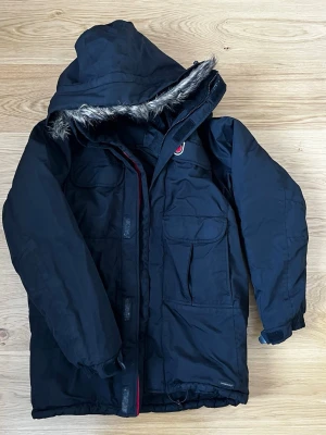 Fjällräven svart parka vinterjacka stl S - En extremt varm och slitstark vinterparkas från Fjällräven. Den är vind- och vattentät med ett foder som håller värmen. Många praktiska fickor inklusive rymliga bälgfickor fram, bröstfickor och innerfickor. Dragsko i midjan och nertill för perfekt passform. Justerbara ärmslut med kardborre.   Jackan är i mycket fint skick och har tagits väl om hand. Dragkedjor och kardborreband fungerar felfritt. Inga synliga skador eller fläckar.  Storlek: S