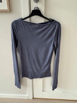 Långärmad topp i blått/grått från Nelly - Säljer en enkel och stilren långärmad topp från Nelly i en snygg grå färg. Toppen har en något bredare halsringning och är gjord i ett mjukt material som sitter tight mot kroppen. Perfekt att matcha med jeans eller kjol.