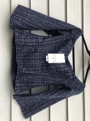 Skit snygg topp från Zara  - Storlek xs/s!Snygg mörkblå kavaj från Zara i tweedmaterial med vitmelerat rutmönster. Kortare modell med markerade axlar och öppen front. Perfekt för att lyfta din outfit med en trendig touch.