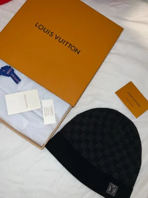 Louis Vuitton svart mössa med rutmönster - Snygg svart mössa från Louis Vuitton med klassiskt rutmönster och vikbar kant. skick 10/10 ingen konstig med den 