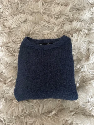 Mörkblå stickad tröja med rund hals - En enkel och stilren mörkblå stickad tröja med rund halsringning. Tröjan har en klassisk passform och ribbstickade detaljer vid halsen. Perfekt för lager-på-lager och passar till det mesta i garderoben.
