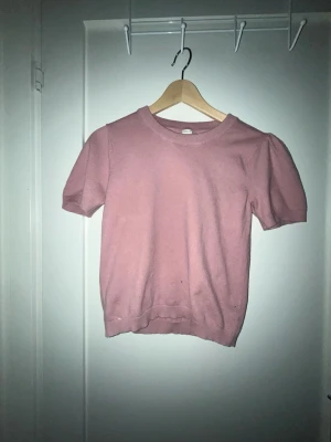 Ljusrosa stickad topp med kort ärm - Söt ljusrosa stickad topp med rund halsringning och korta ärmar. Perfekt till jeans eller kjol för en enkel och stilren look. Mjuk och bekväm, passar dig som gillar en feminin och avslappnad stil. Den har tyvärr en jätteliten svart prick på sig.