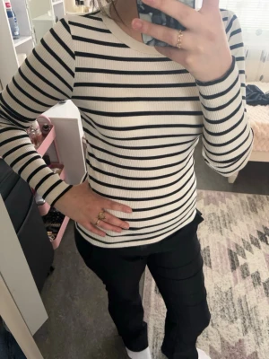 Randig  långärmad topp - Snygg långärmad topp med svarta och vita ränder. Ribbad struktur som ger en tight passform och en klassisk look. Perfekt att matcha med jeans eller kjol för en stilren outfit.