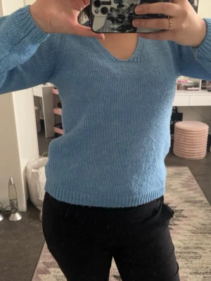 Ljusblå stickad tröja med v-ringning - Mysig ljusblå stickad tröja med v-ringad hals och långa ärmar. Tröjan har en enkel, klassisk design med ribbstickade muddar vid ärmslut och nederkant. Perfekt för att hålla sig varm och snygg under kyliga dagar.