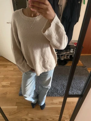 Beige oversized stickad tröja - Mysig beige stickad tröja med avslappnad passform och rund halsringning. Tröjan har långa ärmar och ribbade muddar vid ärmslut och nederkant. Perfekt för lager-på-lager och enkel att matcha med jeans eller kjol.