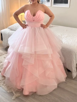 Rosa balklänning - Drömmig långklänning i ljusrosa med flera lager volanger i tyll. Klänningen är axelbandslös med djup v-ringning och markerad midja. Perfekt för bal eller speciella tillfällen när du vill känna dig som en prinsessa.