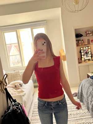 Röd ärmlös topp med fyrkantig hals - Snygg röd topp med fyrkantig halsringning och ärmlös design. Perfekt att matcha med jeans eller kjol för en cool look. Toppens material känns mjukt och stretchigt. Passformen är tight och croppad.