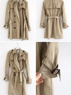 Beige trenchcoat med bälte - Knälång klassisk beige trenchcoat med dubbelknäppning, axelklaffar och bälte i midjan. Jackan har detaljer som spännen vid ärmsluten och stora knappar framtill. Passar perfekt till en person med en längd på ca 158-163 cm. Endast använd ett fåtal gånger. 