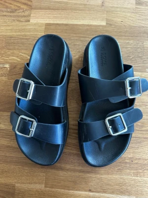 Svarta platåsandaler med spännen - Stilrena svarta sandaler från Soya med två breda remmar och stora silvriga spännen.  Storlek 36!