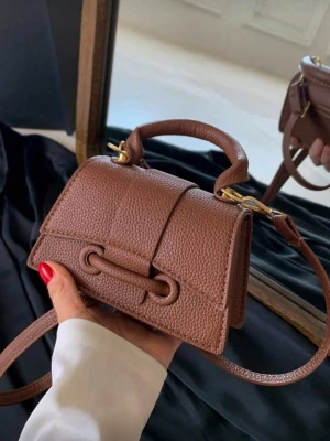 Brun minihandväska i läderlook - Snygg brun minihandväska i strukturerad läderimitation med kort handtag och avtagbar axelrem. Väskan har guldfärgade metalldetaljer och unik knutdetalj framtill. Perfekt för dig som gillar trendiga accessoarer med stilren design.