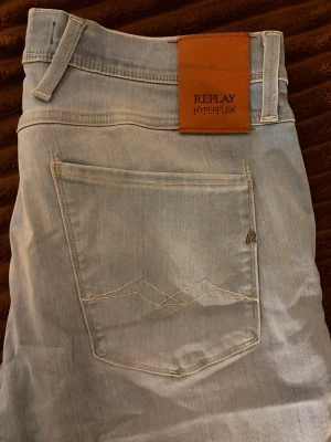 Ljusblå Replay Hyperflex jeans - Säljer ett par ljusblå jeans från Replay Hyperflex med klassisk femficksmodell och snygga sömdetaljer på bakfickan. Jeansen har en skön stretchig känsla och är perfekta för dig som gillar en avslappnad men ändå stilren look.