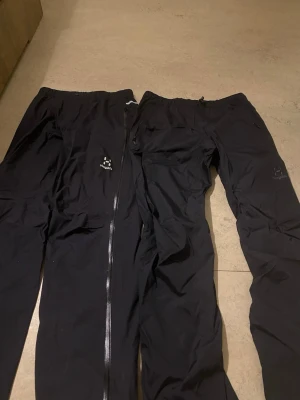 Svarta täckbyxor från Haglöfs - Säljer ett par svarta täckbyxor från Haglöfs med hel dragkedja längs benen. Perfekta för kalla dagar och outdoor-äventyr. Byxorna har en enkel, clean design och är tillverkade i slitstarkt syntetmaterial. Den vita är storlek s , svarta är m båda är helt nya köpt på sommaren 2025 kan tänka mig gå ner i pris ba vid snabb affär 