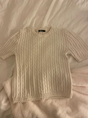 Vit kabelstickad tröja Gina Tricot - Kabelstickad tröja i offwhite från Gina Tricot. Tröjan har korta ärmar, rund halsringning och ribbade muddar vid ärmslut och nederkant. Men den har en liten fläck som knappt syns. Perfekt för lager på lager och enkel att matcha med olika stilar.