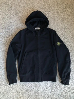 Svart vindjacka från Stone Island - Stone Island Soft Shell-r vindjacka. Jackan har CLG-kod som garanterar äkthet. Passar något litet, S/M. 100% polyester. 