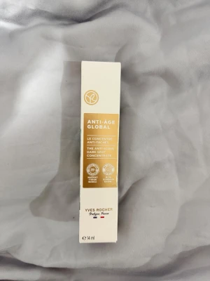 Yves Rocher Anti-Âge Global koncentrat - Anti-Âge Global koncentrat mot pigmentfläckar från Yves Rocher. Kommer i en beige och vit förpackning, 14 ml. Innehåller växtbaserade ingredienser och är framtagen för att minska synligheten av mörka fläckar och ge en jämnare hudton.