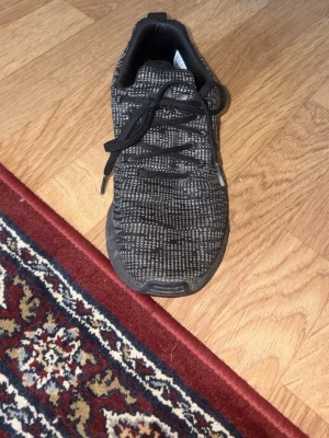 Svartmönstrad sneaker med stickad ovandel - Snygg svart sneaker med grått mönster och stickad ovandel. Skon har svarta skosnören och en låg profil som ger en sportig vibe. Perfekt för dig som gillar en stilren och modern look. Sulan är svart och skon är lätt och flexibel.