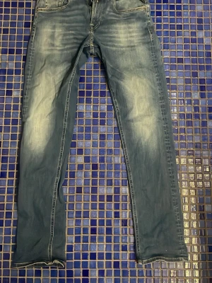 Blå slim fit jeans - Säljer ett par blå Replay hyperflex slim fit jeans med snygga och tvättade detaljer på benen. Klassisk femficksmodell med kontrastsömmar och normal midja. Jeansen har en modern look och passar perfekt till en avslappnad stil.