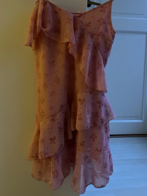 Rosa volangklänning med blommönster - Söt rosa klänning med volanger och blommigt mönster. Klänningen har asymmetrisk axel och flera lager volanger som ger en romantisk känsla. Perfekt för dig som gillar en feminin och trendig stil. Är i barn stolek! Använd ca 2 gånger och stoleks lappen är borta men är ca 140. Pris kan diskuteras
