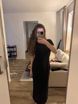 Svart långklänning med kort ärm - En stilren svart långklänning med korta ärmar och rak passform. Klänningen har en enkel design utan mönster eller detaljer och passar perfekt för dig som gillar minimalistiskt mode. Materialet ser ut att vara mjukt och följsamt.