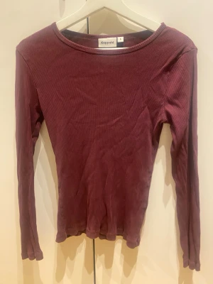 Vinröd ribbad långärmad topp Kappahl - Vinröd långärmad topp från Kappahl i ribbad bomull. Modellen har en rund halsringning och sitter tight mot kroppen. Perfekt att styla med jeans eller kjol för en enkel och snygg look.