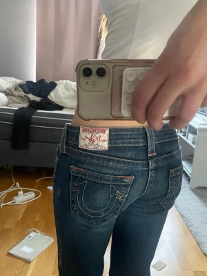 True Religion mörkblå jeans - Säljer ett par mörkblå jeans från True Religion med ikoniska kontrastsömmar och snygga fickdetaljer bak. Klassisk femficksmodell med låg midja och utsvängda ben. De är i mycket bra skick.